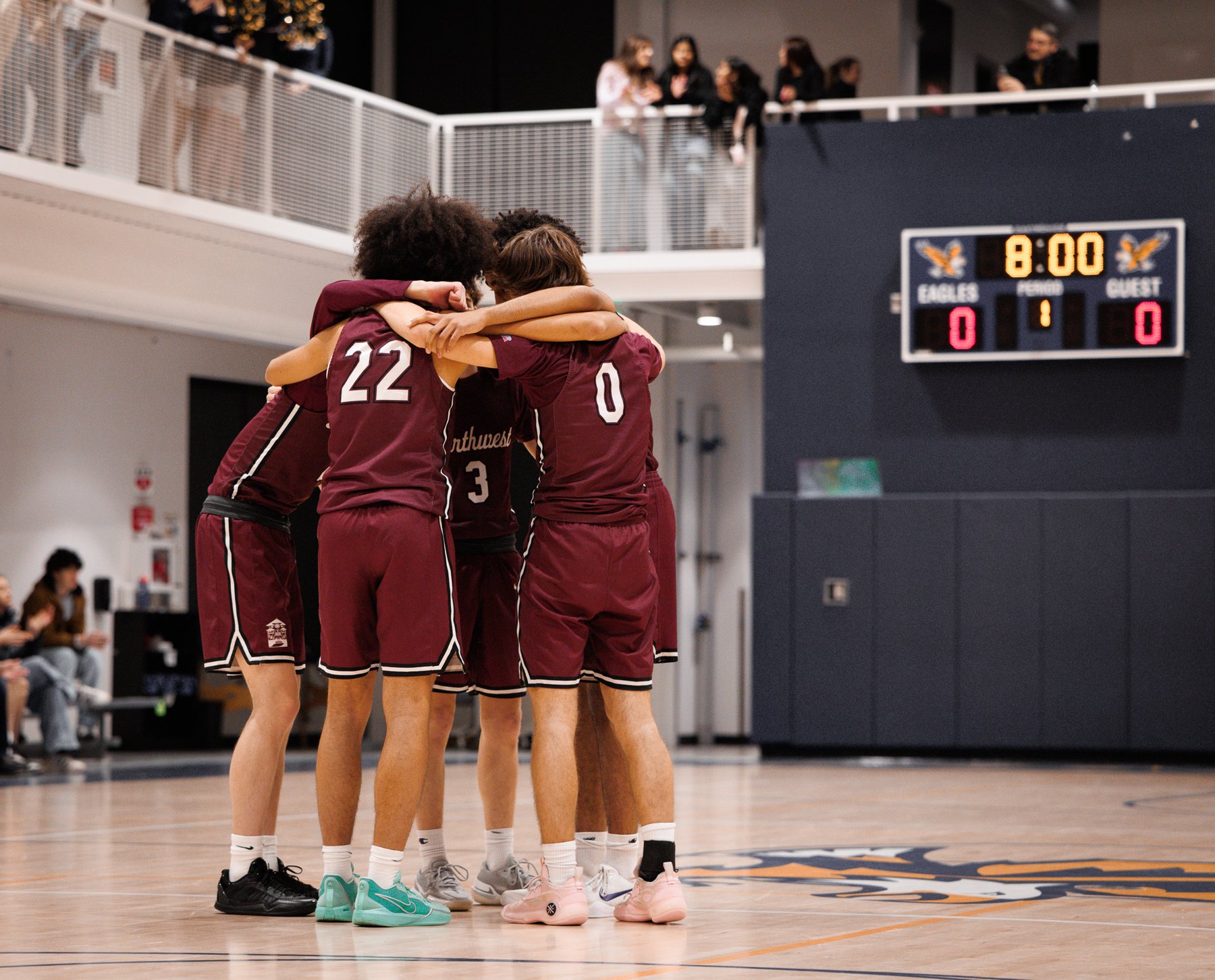 High school basketball team huddled at center court before tip-off, scoreboard reading 8:00