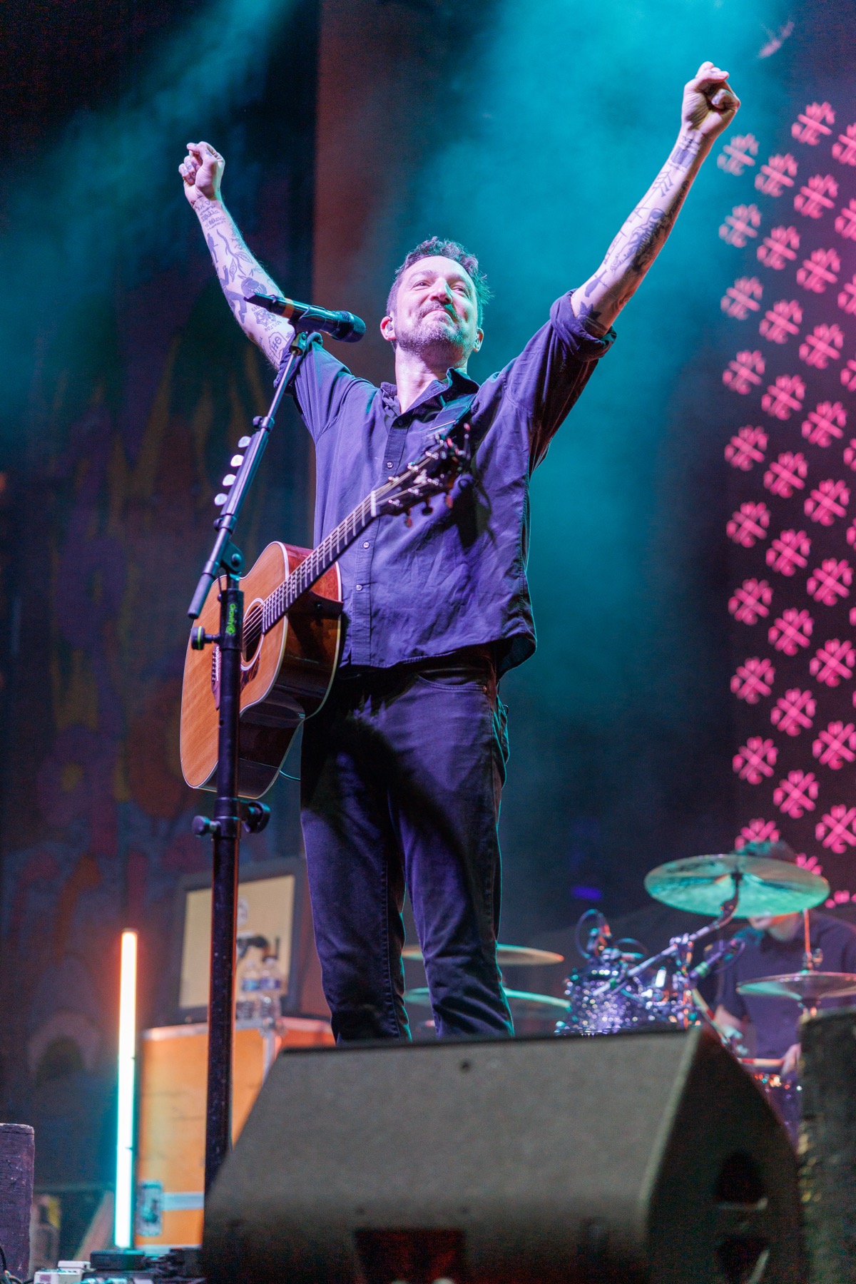 Frank Turner with guitar strapped on, both arms raised in the air on stage